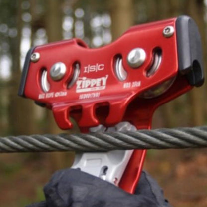 An ISC Zippey Clip 'n Zip Trolley attached to a zip line cable, with a robust red casing and dual pulleys, designed for smooth and efficient travel on zip lines in adventure parks